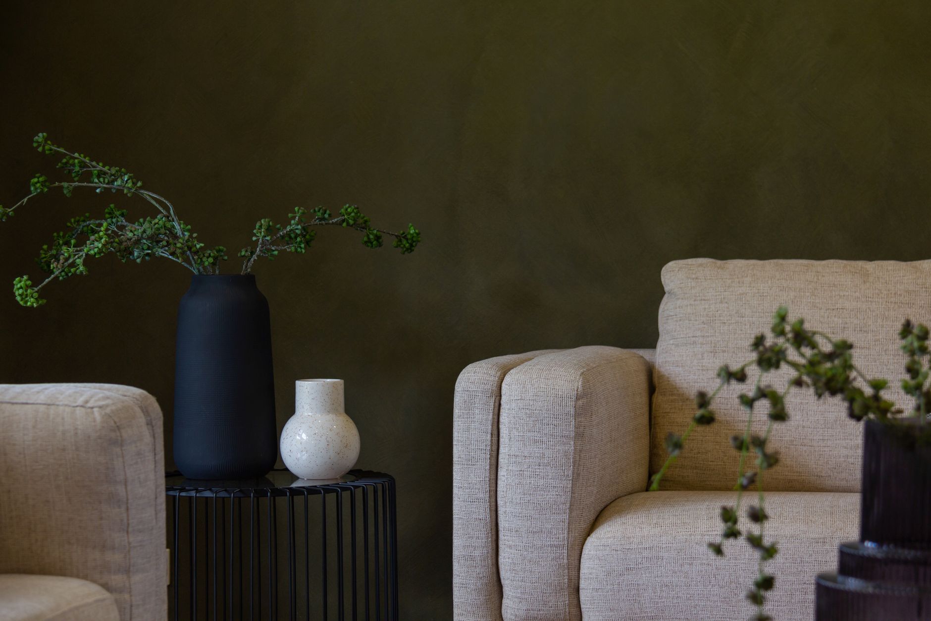 Woonkamer met diepgroene wand, lichte fauteuils en een zwarte vaas